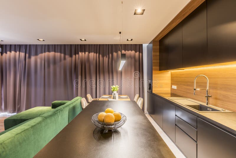 Real photo of metal bowl with artificial yellow fruits placed on black countertop in dark modern kitchen interior