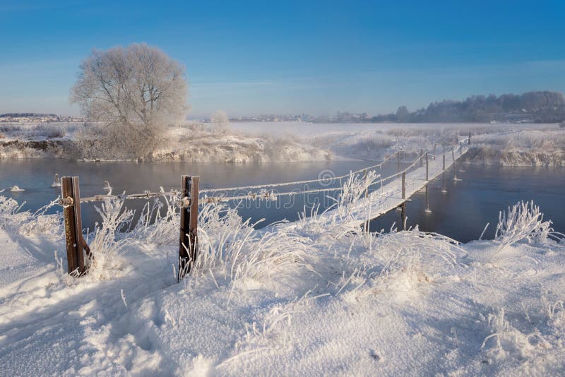 Real Russian Winter. Winter Landscape With Trail Across The Dangerous Rural Suspension Bridge Over The Snowy Foggy River