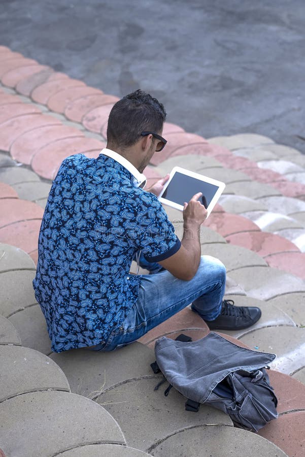Rear Image of Young Man Sitting on Bleachers Using a Tablet Stock Image
