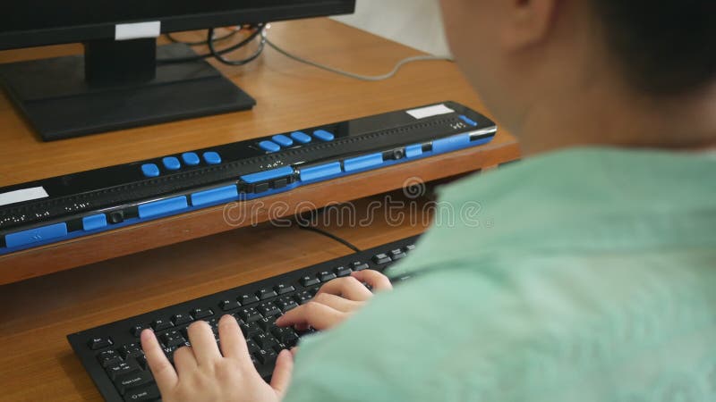 Rear view of blind person woman using computer keyboard and braille display or braille terminal a technology assistive device for