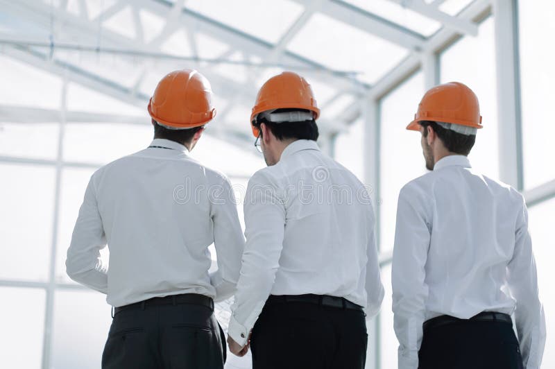 Rear view.businessmen in protective helmets standing in the new office royalty free stock photo Rear view.businessmen in protective helmets standing in the new office royalty free stock photo