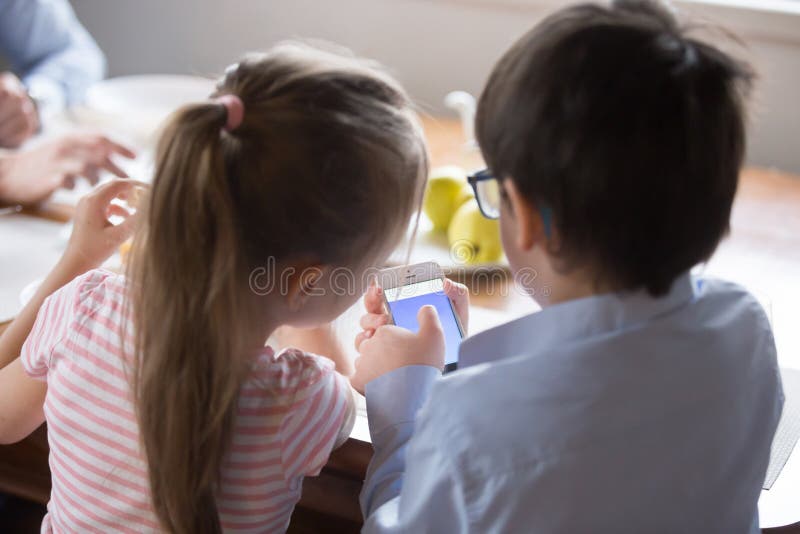 Rear view children using smartphone sitting in the kitchen royalty free stock photo Rear view children using smartphone sitting in the kitchen royalty free stock photo