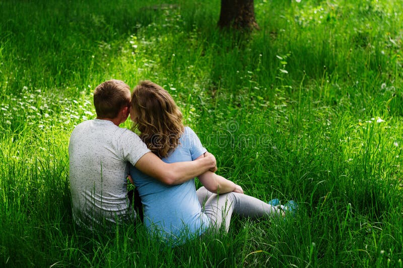 Молодые люди обнимаются в траве. Пара сидит на траве. Два человека сидят на траве. В траве сидел.