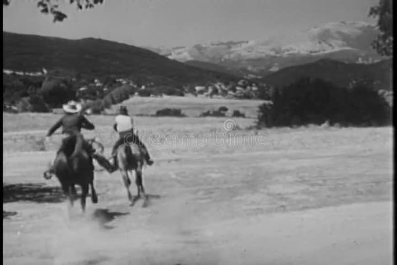 Rear view of cowboys on horses galloping through prairie land