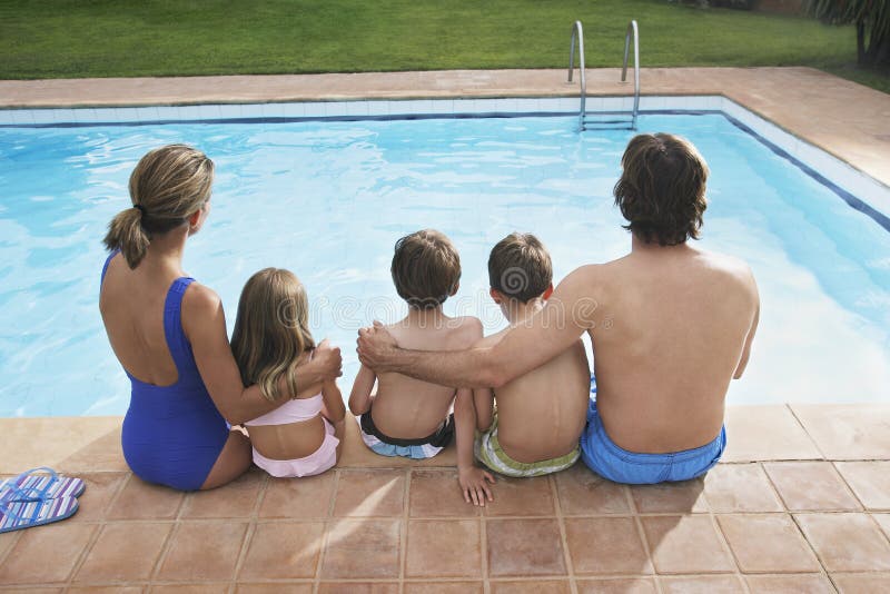 Rear View Of Family Sitting By Pool