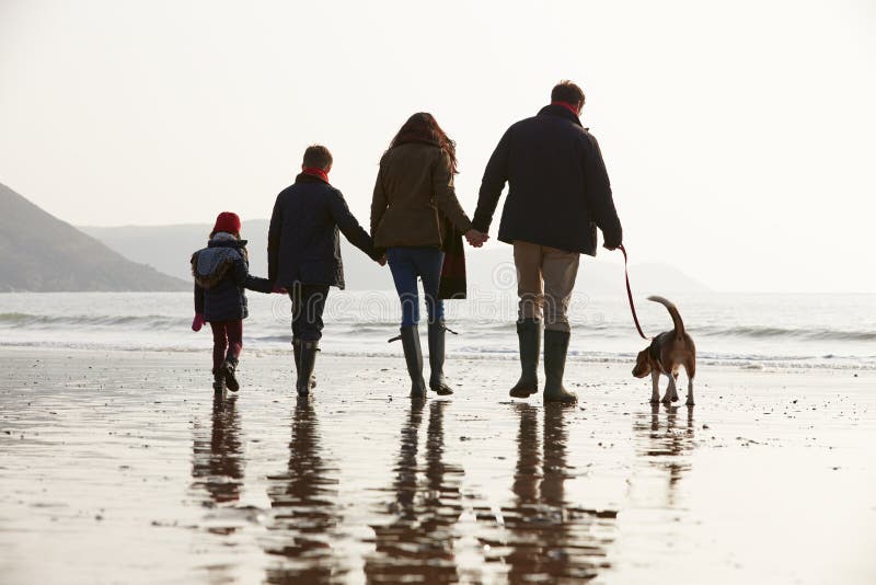 Rear View Of Family Walking Along Winter Beach With Dog