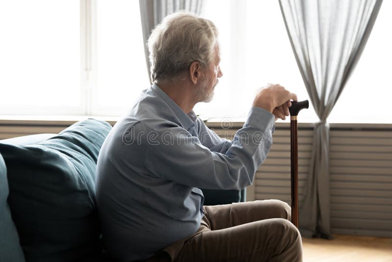 Rear view lonely mature man holding cane sitting on couch