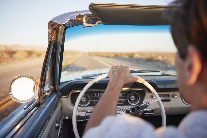 Rear View Of Man On Road Trip Driving Classic Convertible Car Towards Sunset