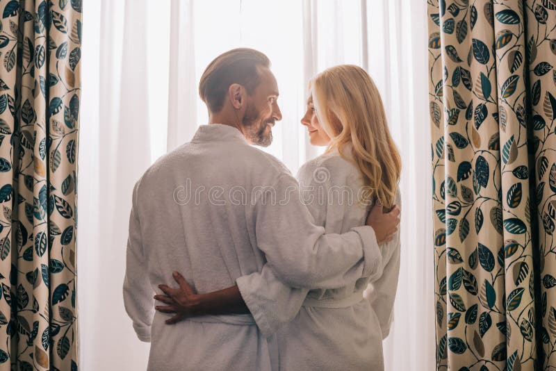 rear view of middle aged couple in love wearing bathrobes and smiling each other in hotel stock photo rear view of middle aged couple in love wearing bathrobes and smiling each other in hotel stock photo