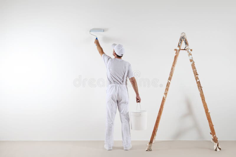 Rear view of painter man painting the wall, with paint roller and bucket, on big empty space with wooden ladder