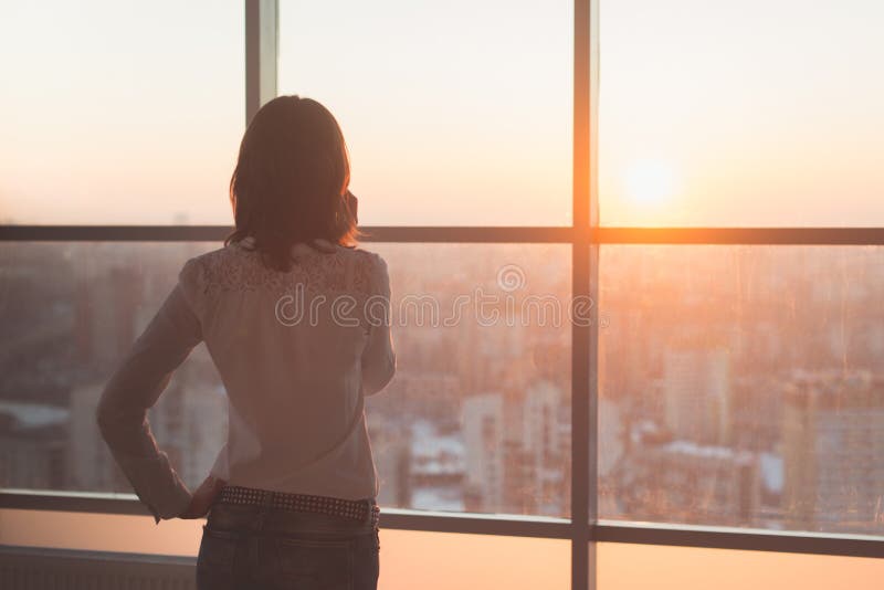 Rear view portrait of young worker speaking using cell phone, looking out the window. Female having business call, busy