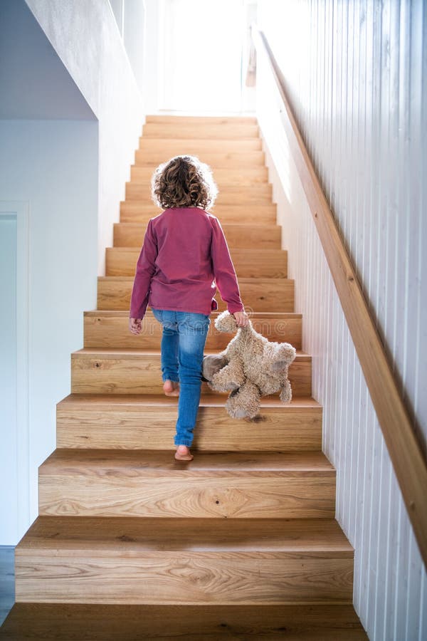 A rear view of small girl walking up wooden stairs indoors at home.