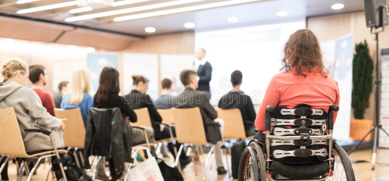 Rear view of unrecognizable woman on a wheelchair participating at business conference talk.