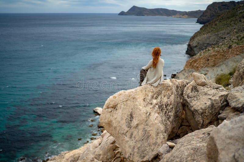 Rear view of woman looking at sea while sitting on rock