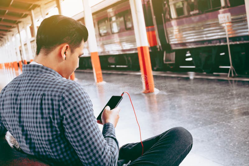 Rear view of young asian hipster man holding mobile phone using