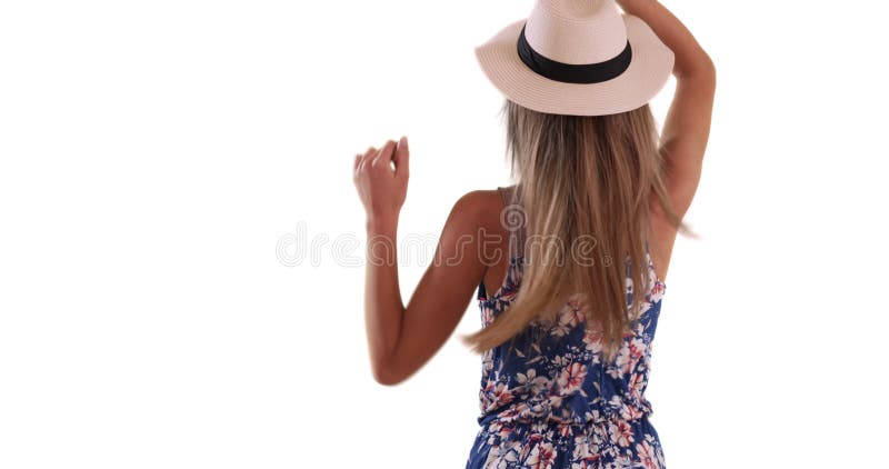 Rear view of young lady taking off hat and letting hair flow on white backdrop