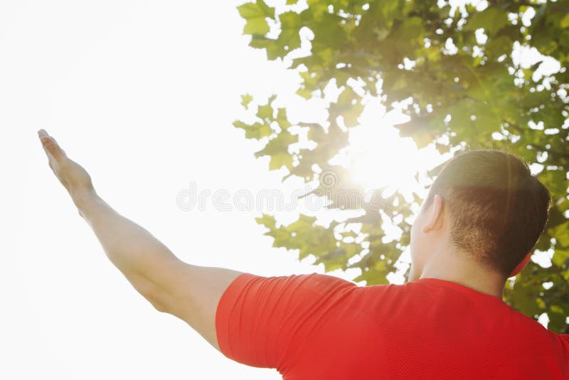 Rear view of young muscular man stretching by a tree, hand and arm raised towards the sky and the sun in Beijing, China stock photo Rear view of young muscular man stretching by a tree, hand and arm raised towards the sky and the sun in Beijing, China stock photo