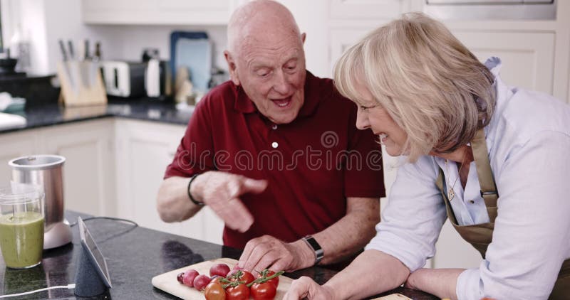 Recepttablett online och pensionerat lyckligt par i köksmatlagningslunch med hälsosam mat och vegetabilisk kost. Gammal stock video