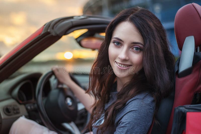 Recht junge Brunettefrau, die rotes Cabrioletluxusauto bei dem Sonnenuntergang fährt lizenzfreies stockfoto Recht junge Brunettefrau, die rotes Cabrioletluxusauto bei dem Sonnenuntergang fährt lizenzfreies stockfoto