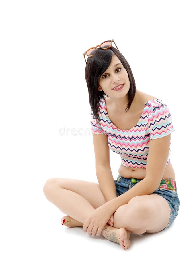 Recht junges Brunettefrauensitzen im Schneidersitz auf Weiß lizenzfreie stockfotos Recht junges Brunettefrauensitzen im Schneidersitz auf Weiß lizenzfreie stockfotos