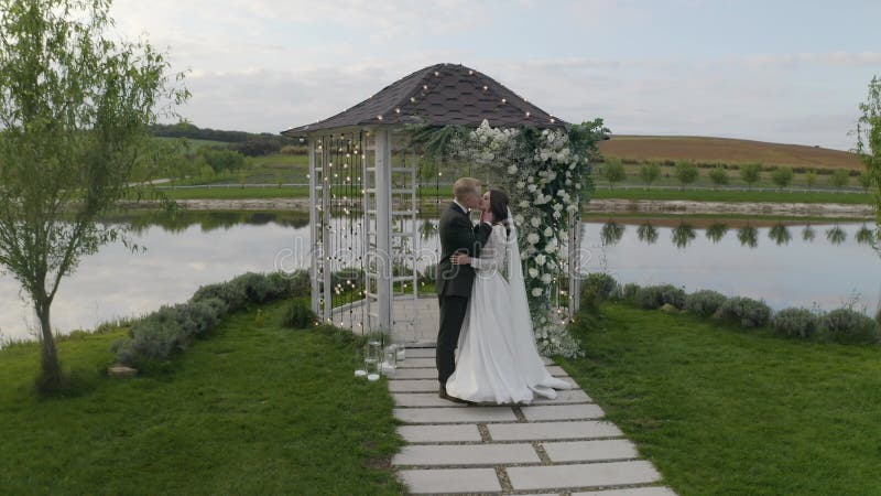 Recién casados novio novia abrazando abrazos besando arco de ceremonia matrimonial de boda con flores