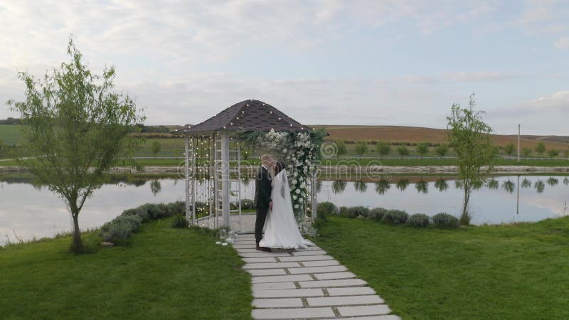 Recién casados novio novia abrazando abrazos besando arco de ceremonia matrimonial de boda con flores