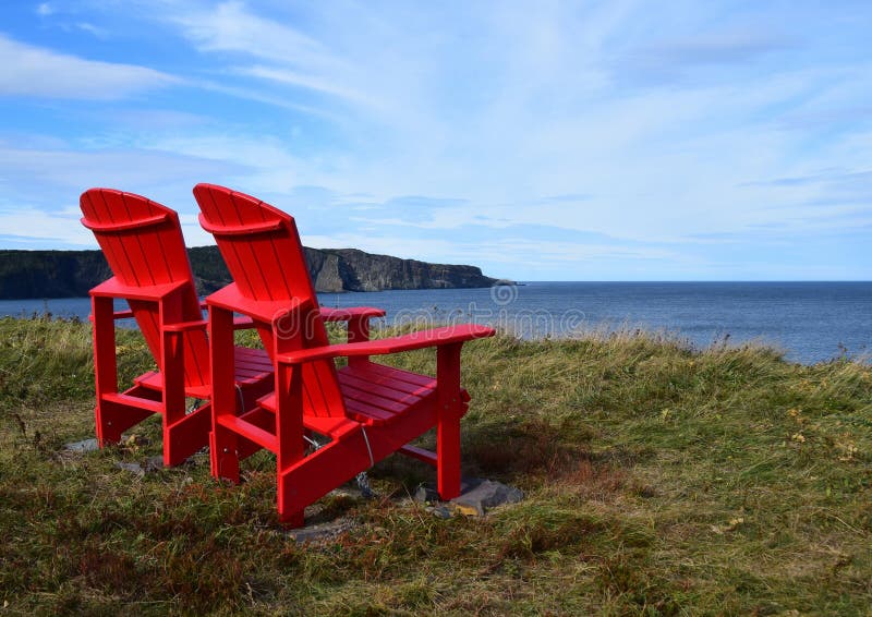 Red Adirondack chairs on the edge of a cliff overlooking the ocean