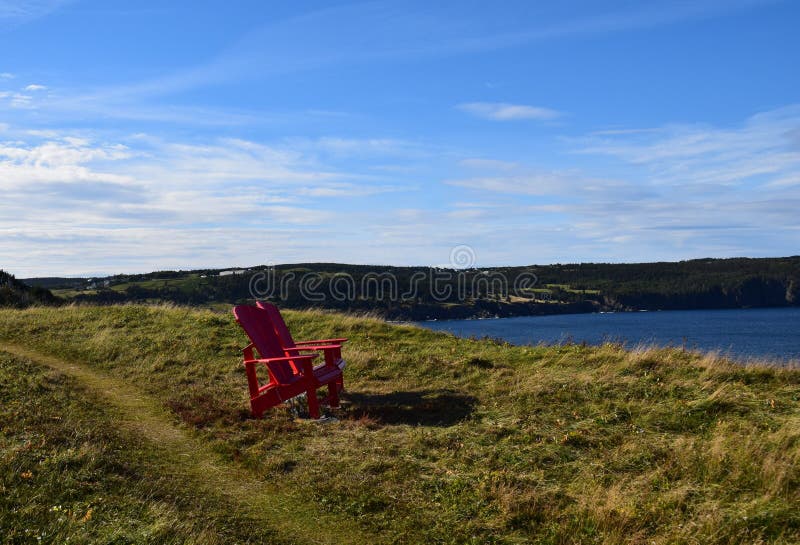 Red Adirondack chairs on the edge of a cliff overlooking the ocean