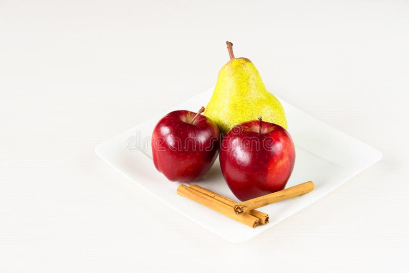 Red apples, green pear and cinnamon in white plate on white wooden background. royalty free stock image