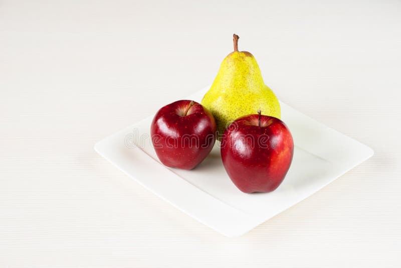 Red apples, green pear in white plate on white wooden background. stock photo
