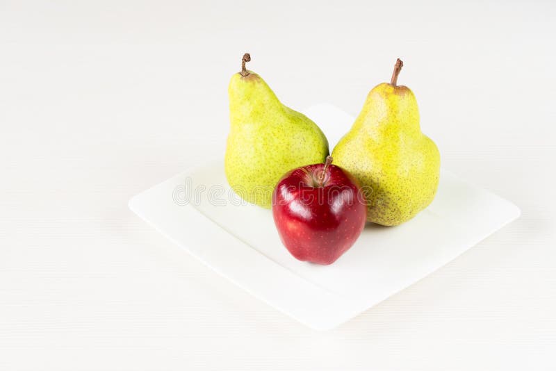 Red apples, green pear in white plate on white wooden background. stock photos