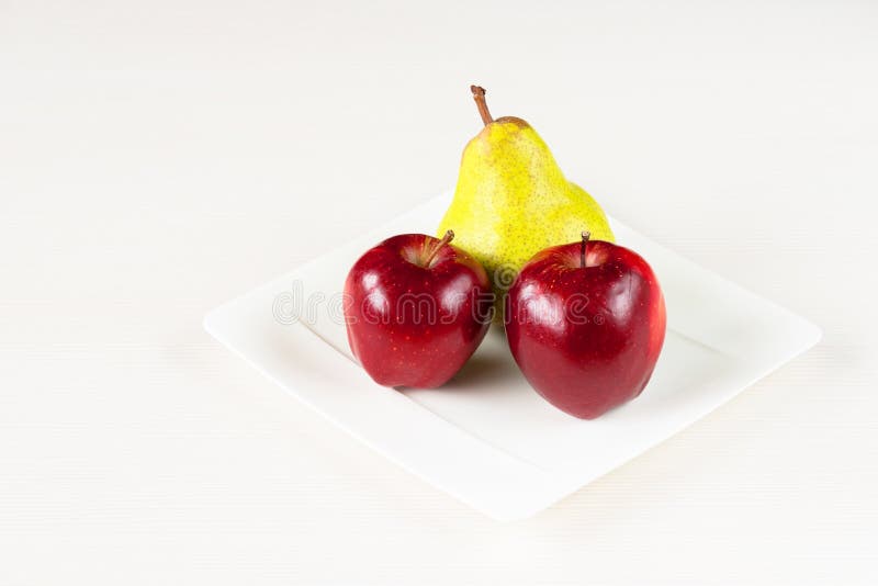 Red apples, green pear in white plate on white wooden background. royalty free stock image