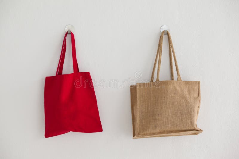 Red and beige fabric bags hanging on self adhesive hook on white wall. Red and beige fabric bags hanging on self adhesive hook on white wall