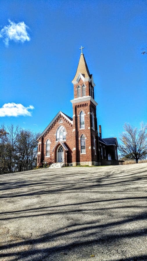 A beautiful red, brick church with large steeple and stained glass windows with a bunch of shadows from nearby trees in the parking lot in front of the church. A beautiful red, brick church with large steeple and stained glass windows with a bunch of shadows from nearby trees in the parking lot in front of the church.