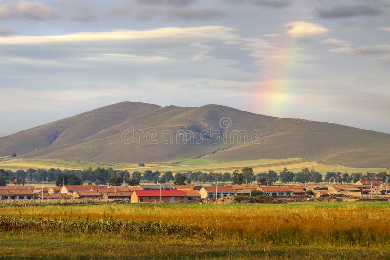 Mattone silenzioso case raccolti un secondo prato montagna, arcobaleno Attraverso tramonto il cielo.