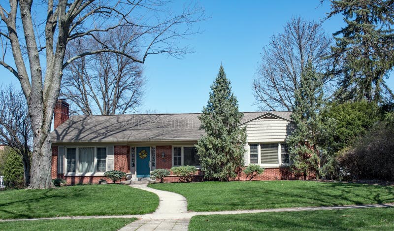 Red brick, ranch house with curving sidewalk surrounded by deciduous and evergreen trees. Red brick, ranch house with curving sidewalk surrounded by deciduous and evergreen trees.