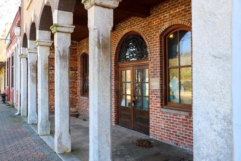 A red brick store front with concrete pillars and arches and arched windows with brown wooden trim in Douglasville