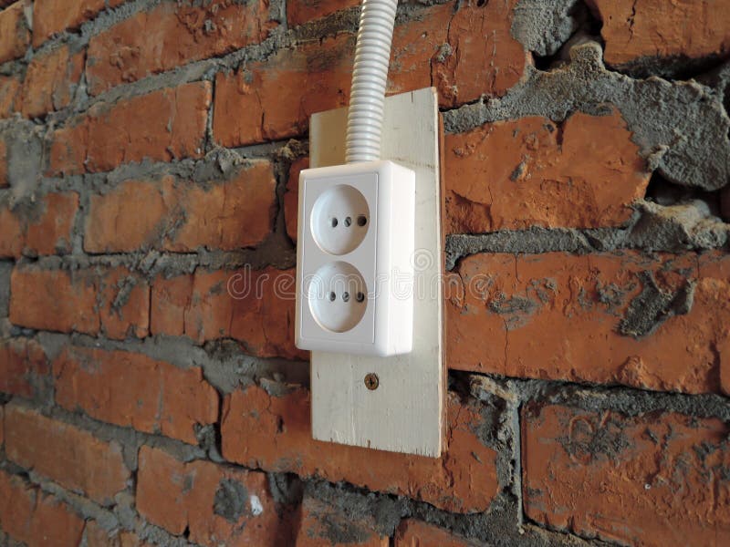 Red brick wall with white electrical plug socket in garage