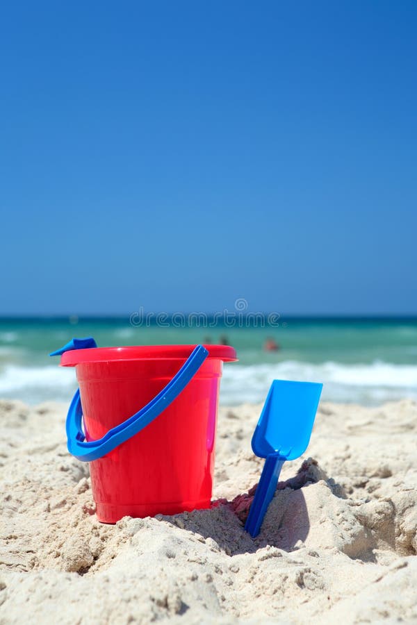 Red bucket and blue spade on sunny, sandy beach