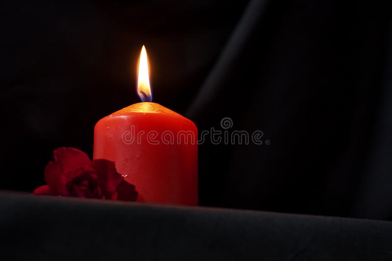 A red burning candle and a red rose on a black background copy space gothic style