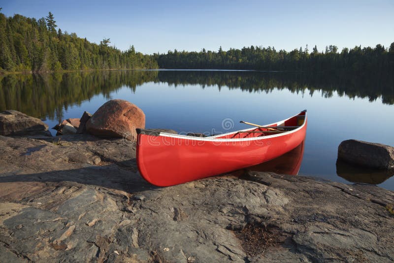 Red Canoe on Rocky Shore of Calm Lake with Pine Trees