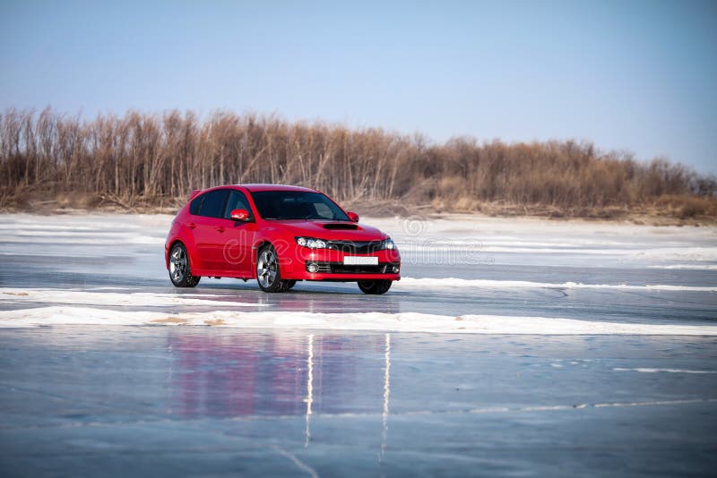 Red car moving by ice of frozen river