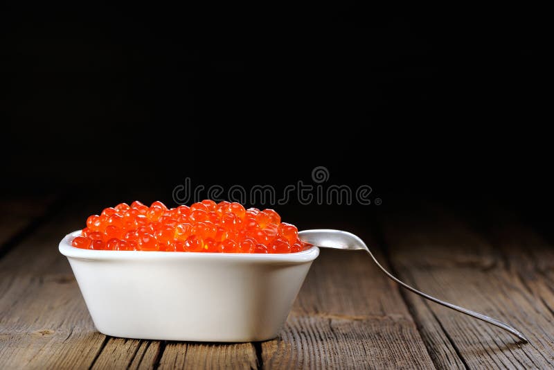 Red caviar in white bowl with silver spoon on wooden background