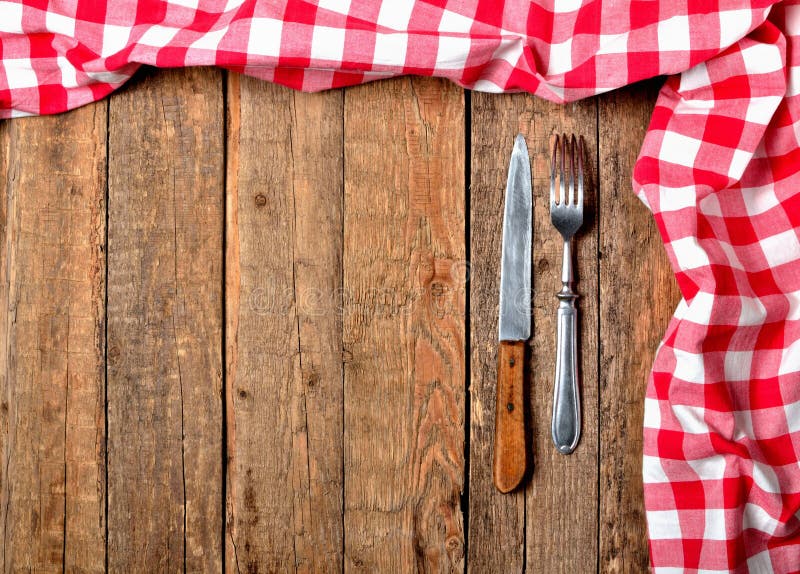 Red checkered tablecloth top and right frame, knife and fork on vintage wooden table background - view from above