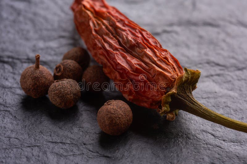 Red Pepper in the Company of Allspice Black Pepper Macro Stock Photo