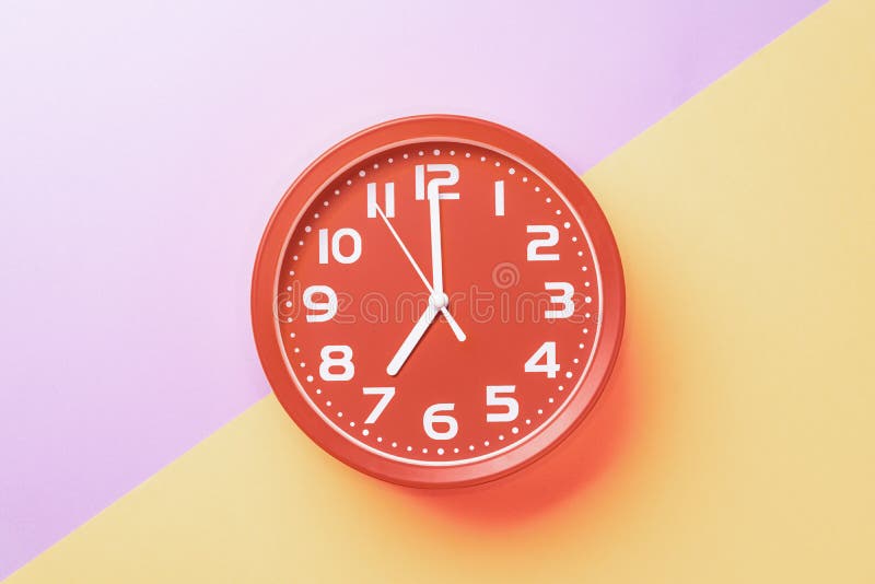 Red Clock Showing Seven O`clock With White Numbers On A Yellow Lilac