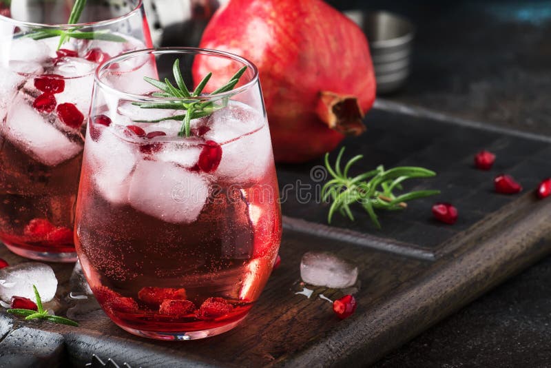 Red cocktail with cold vodka and pomegranate juice, ice cubes and rosemary, bar tools, blue black bar counter background, copy