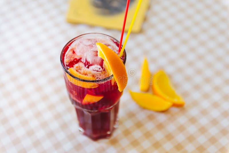 Red cocktail with straws and orange wedge in high glass