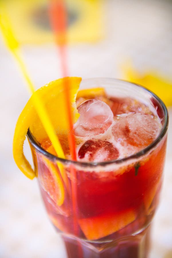 Red cocktail with straws and orange wedge in high glass