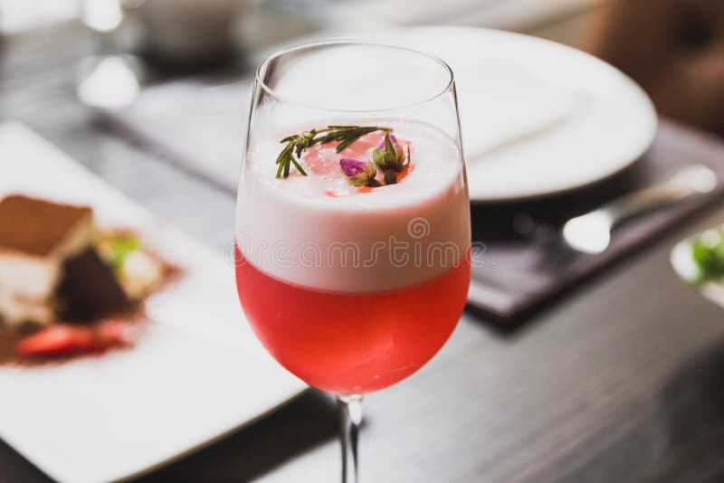 Red Cocktail in Wine Glass Topping with Foam, Flowers and Rosemary